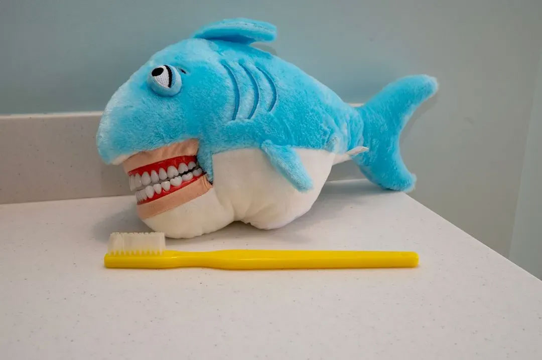 A stuffed shark toy with an open mouth, sitting on a table next to a toothbrush.
