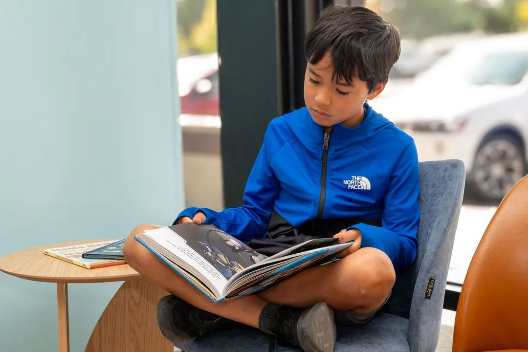 A young boy sitting on the floor, engrossed in reading a book.