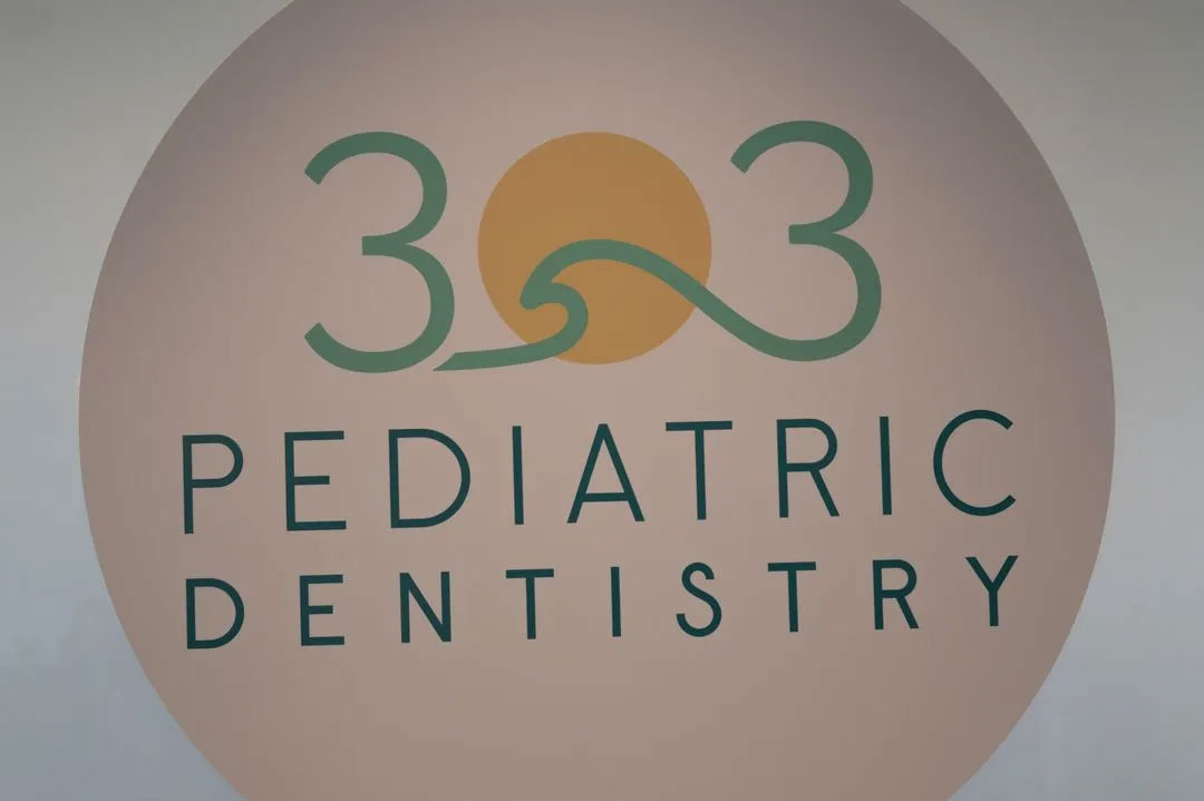 The image displays a logo with text that reads  303 PEDIATRIC DENTISTRY  set against a backdrop featuring a circular emblem with a sunburst design, and below the text is the graphic representation of a toothbrush with bristles.