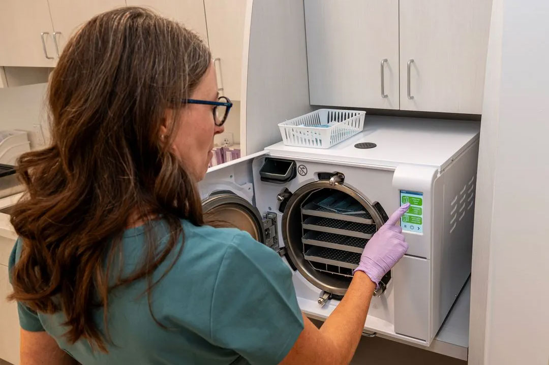 Woman in scrubs inspecting laundry machine with digital display.